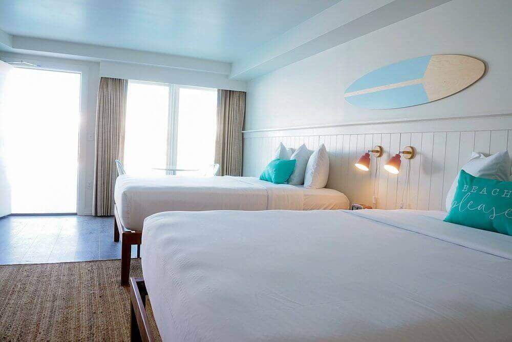 Coastal-style room with two beds, teal pillows, and surfboard art, perfect for a seaside retreat.