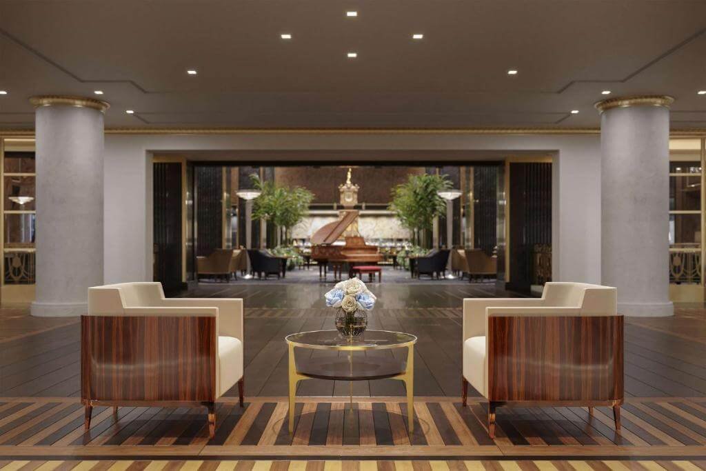 Luxurious lobby with wooden chairs, glass table, grand piano, and greenery in the background.
