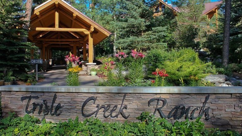Scenic Triple Creek Ranch entrance with wooden lodge, vibrant flowers, and lush greenery.