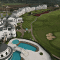 Aerial view of a luxury golf resort with castle architecture, pools, and green fairways.