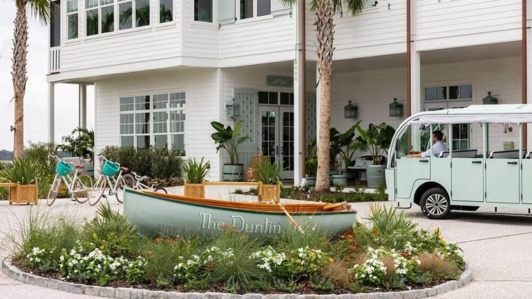 The dunlin auberge resorts collection Luxury hotel The Dunlin with boat, bikes, and shuttle in tropical setting, palm trees, white building, lush garden.